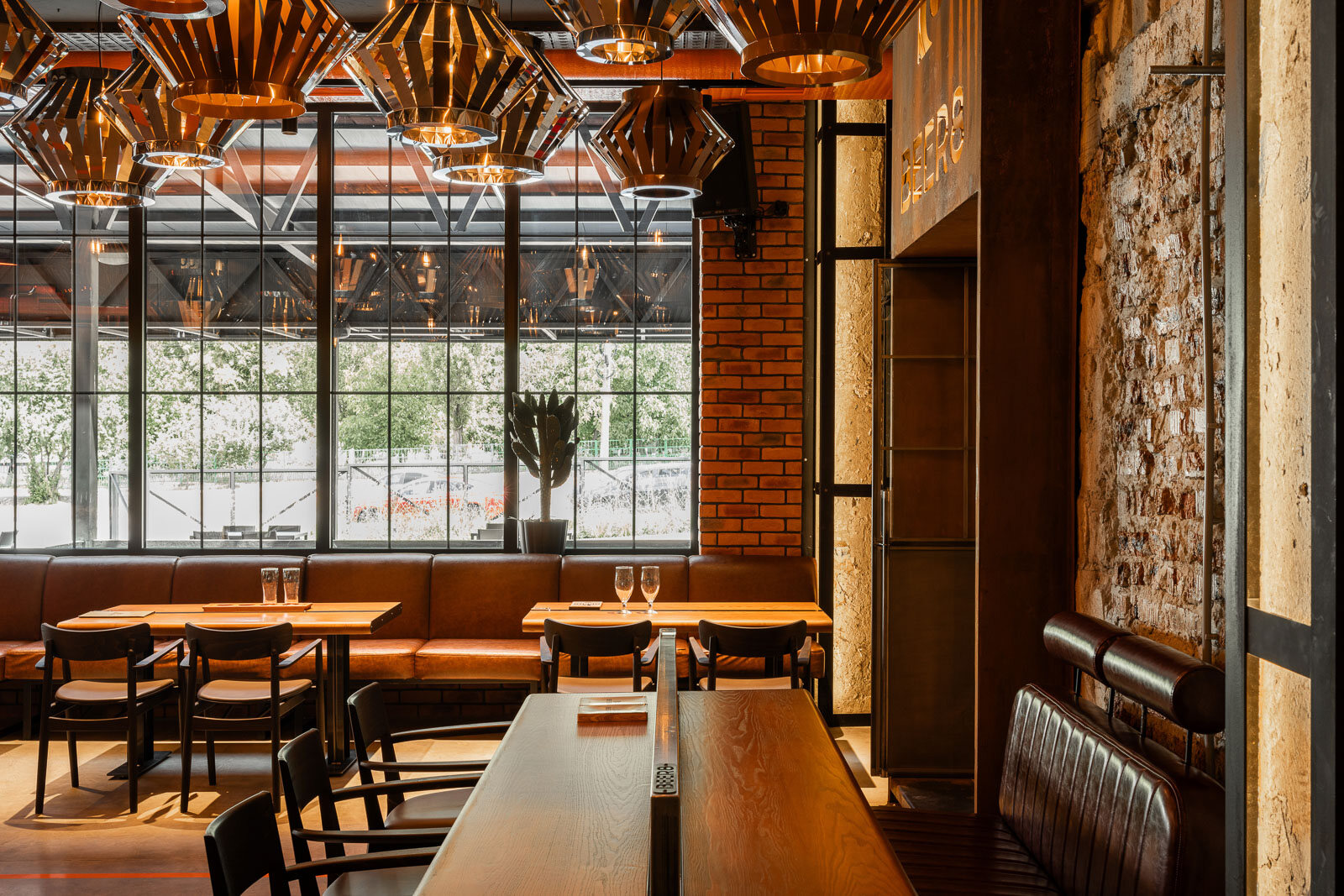 Sala principală a pub-ului craft Beer 8 din Bălți, cu mese comune de lemn, pendule geometrice, structură industrială la vedere și un mural cu hipopotam pe fundal de cărămidă