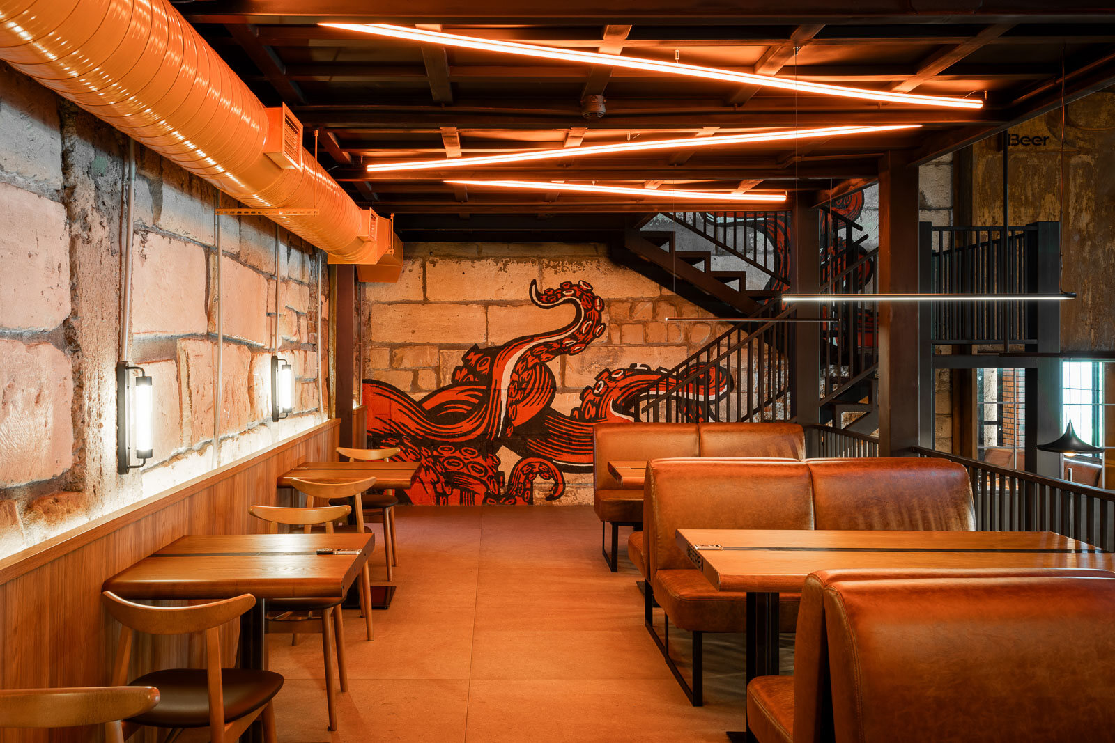 Salon Beer 8 cu corpuri liniare portocalii pe tavan și pereți de cărămidă, separeuri din piele și un mural grafic