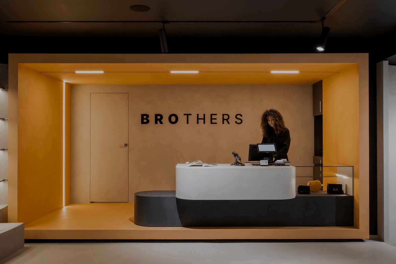 Zona de recepție Brothers cu sigla pe perete, nișă cu accent de culoare cald și tejghea curbată
