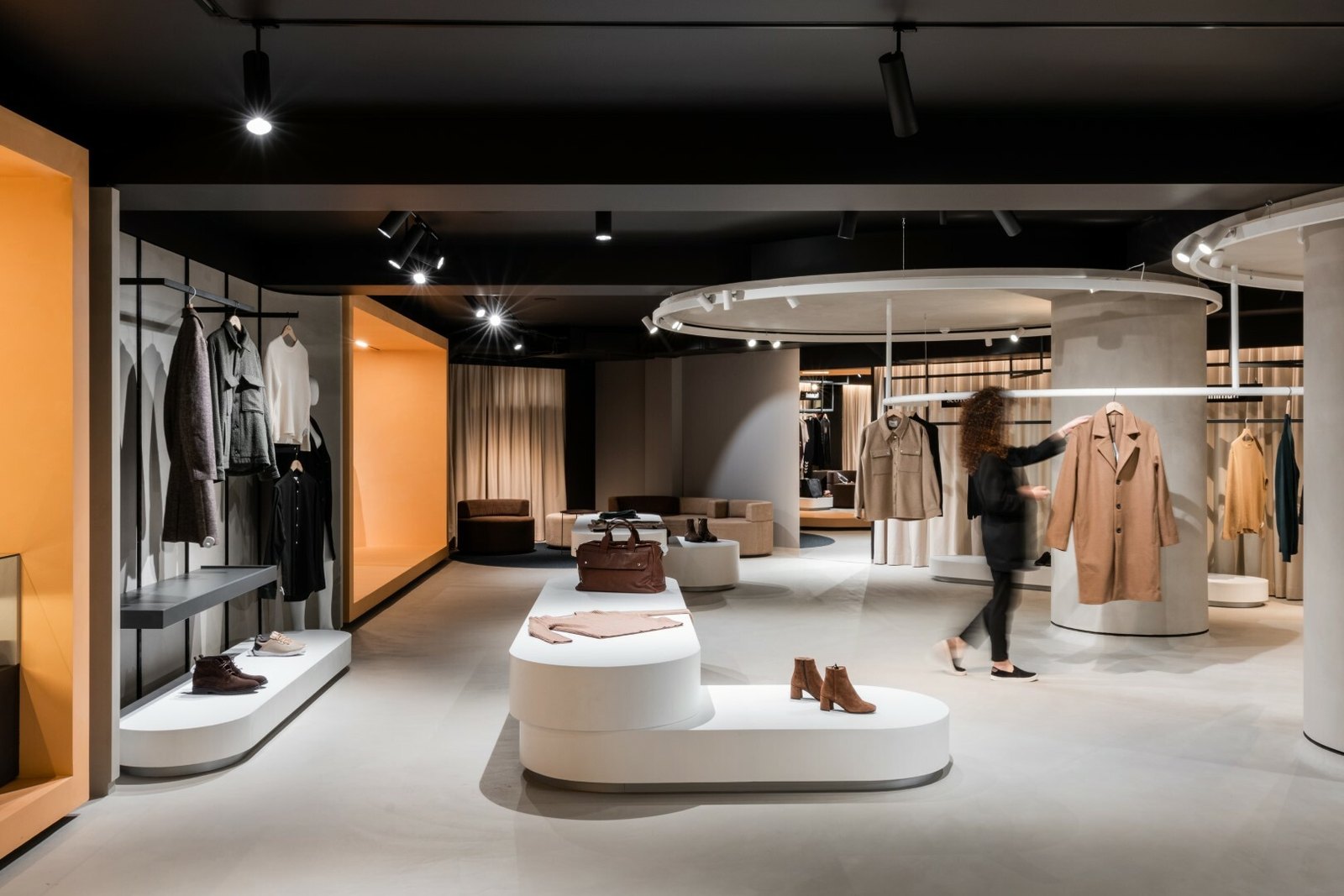 Zonă de expunere în Brothers cu proiectoare pe șină peste manechine și haine, inel de lumină pe fundal